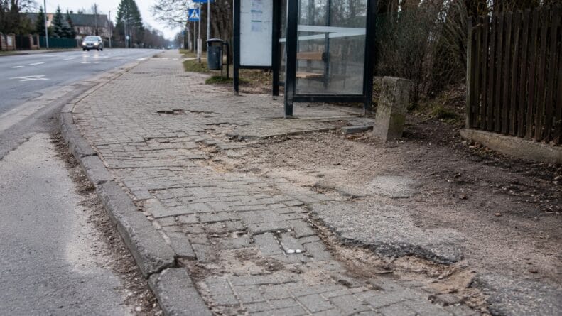 Zniszczony chodnik przy przystanku autobusowym wymagający naprawy.
